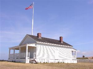 Color photograph of a white plank building with an American flag flying in front of it