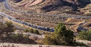 Photo of cars lined up on road with mountain in background and bushes in foreground.