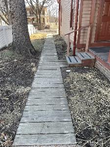 Photo of a wooden boardwalk along the side of a wooden sided house near a fence