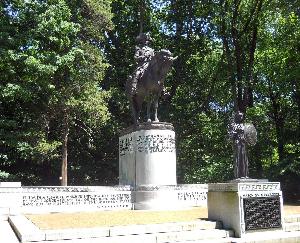 In a clearing surrounded by tall trees, the Nathanael Greene Monument features two bronze statues, the larger of which is Nathanael Greene on a stallion standing on a tall pedestal. The smaller figure is the Greek goddess Athena with a shield and laurels.