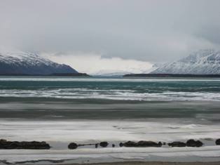 The snow covered ridges of Mt. La Gorce (left background) and Mt. Katolinat (right background) as seen from the icy shore of Naknek Lake at Brooks Camp on the afternoon of 5 May 2008. Photograph taken by Daniel Noon.