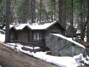 Photo of a cabin in Curry Village in the winter surrounded by snow and large rocks. 