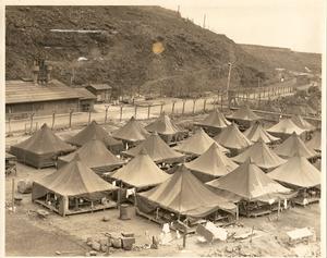 A photo of the historic Honouliuli site with makeshift tents set at the base of a hill next to a dirt road. Photo courtesy of Hawai'i's Plantation Village.