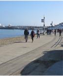 Park visitors walking west along the Promenade. The Aquatic Park bleachers at to the right, the Park's Hyde Street Pier is at left, in the distance.