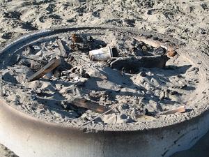 Current Ocean Beach fire ring filled with sand and partially burned debris.