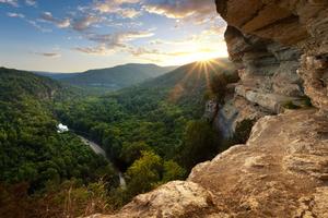 Photo of low sun over the Buffalo River from a high vantage showing rock bluffs and leafy trees.