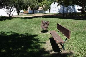 Photo of Legacy Gardens showing old bench & trash can in area where picnic tables will go.