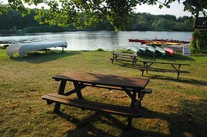 Picnic table by the river with kayaks sitting on the banks with the sun setting.