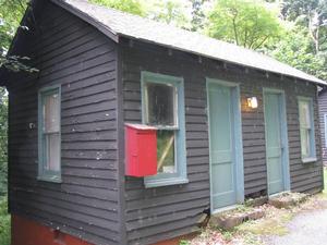 A photo of Cottage B, which is a side-gabled building, with brown horizontal siding. There are two green doors and two vertical windows on the front facade. 