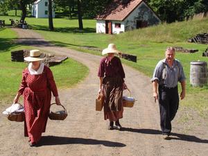 Photo of three people in 19th century costume walking on village road