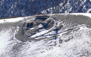 This aerial photograph shows infrastructure currently on the summit of Rogers Peak: a gravel road, solar panels, three buildings, propane tanks, and two telecommunications towers.