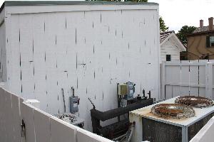Color photo of an exterior HVAC unit next to a white shed/barn.
