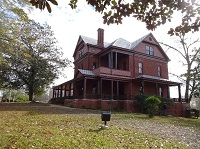 Photo of the the Oaks, a three-story Queen Anne style home brick home with grassy lawn and trees