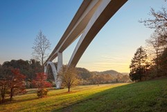 White bridge with curved arch spanning valley with trees on both sides.