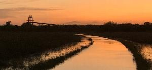 This is a photograph of the Shark Valley Tram Road. In the foreground, a flooded Tram Road is flanked by marshes. The Shark Valley Tower with brilliant red and orange sunset colors can be seen in the background.