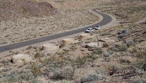 Photo looking down at circular tanks at Journigan's Mill, the paved Emigrant Canyon Road, and two vehicles parked on the shoulder.