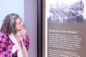 A person looks at a museum exhibit panel containing a historic photo and text under the heading, "Adventure or Fool's Mission?"